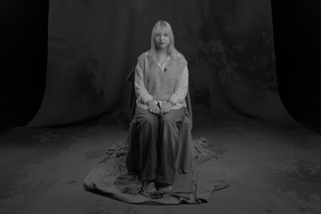 A young woman sitting on a chair in a seemingly gloomy and empty studio